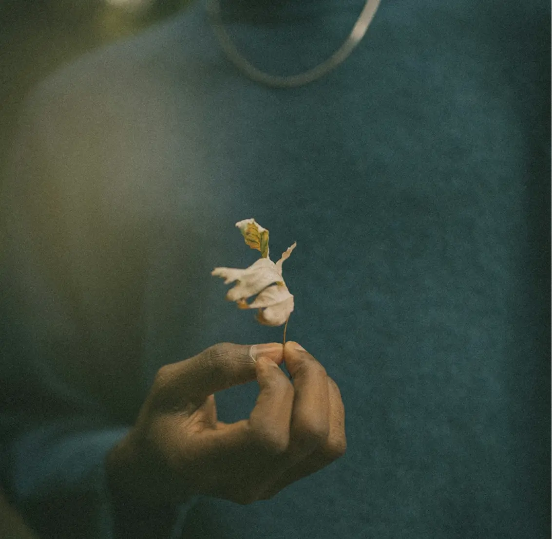 someone holding a tiny flower in their hand with a necklace