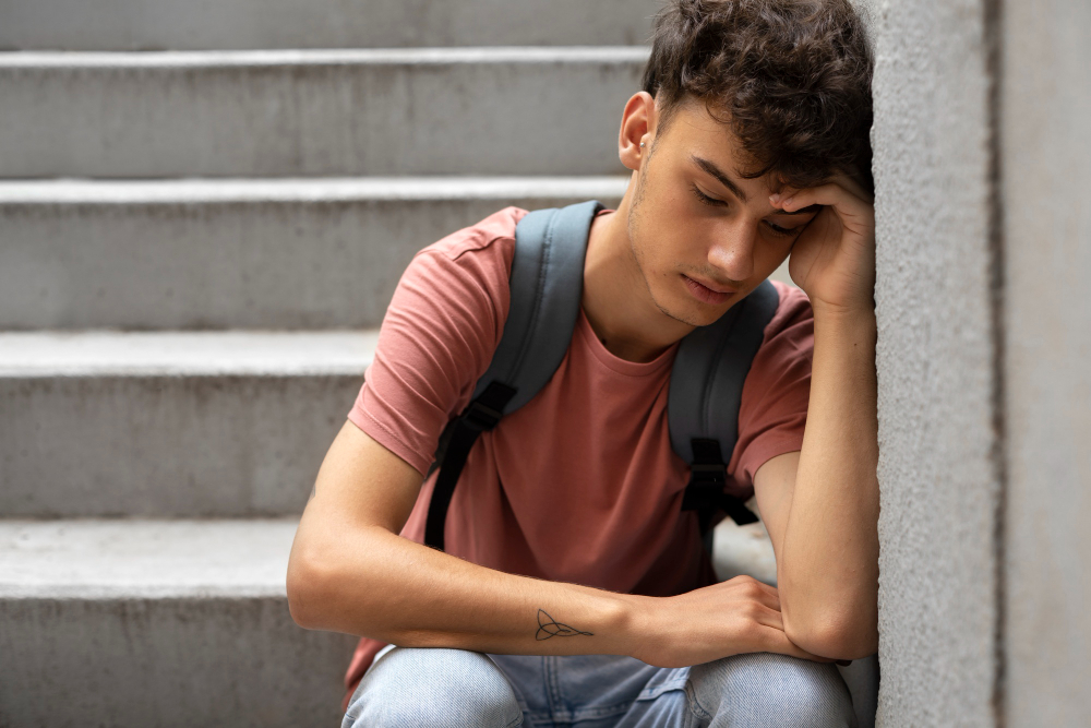 Sad teenage boy sitting on stairs while experiencing signs of teen anxiety.