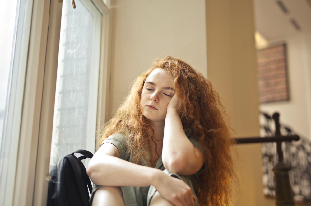 Tired teenager sitting in a school hallway while experiencing signs of anxiety in teens.